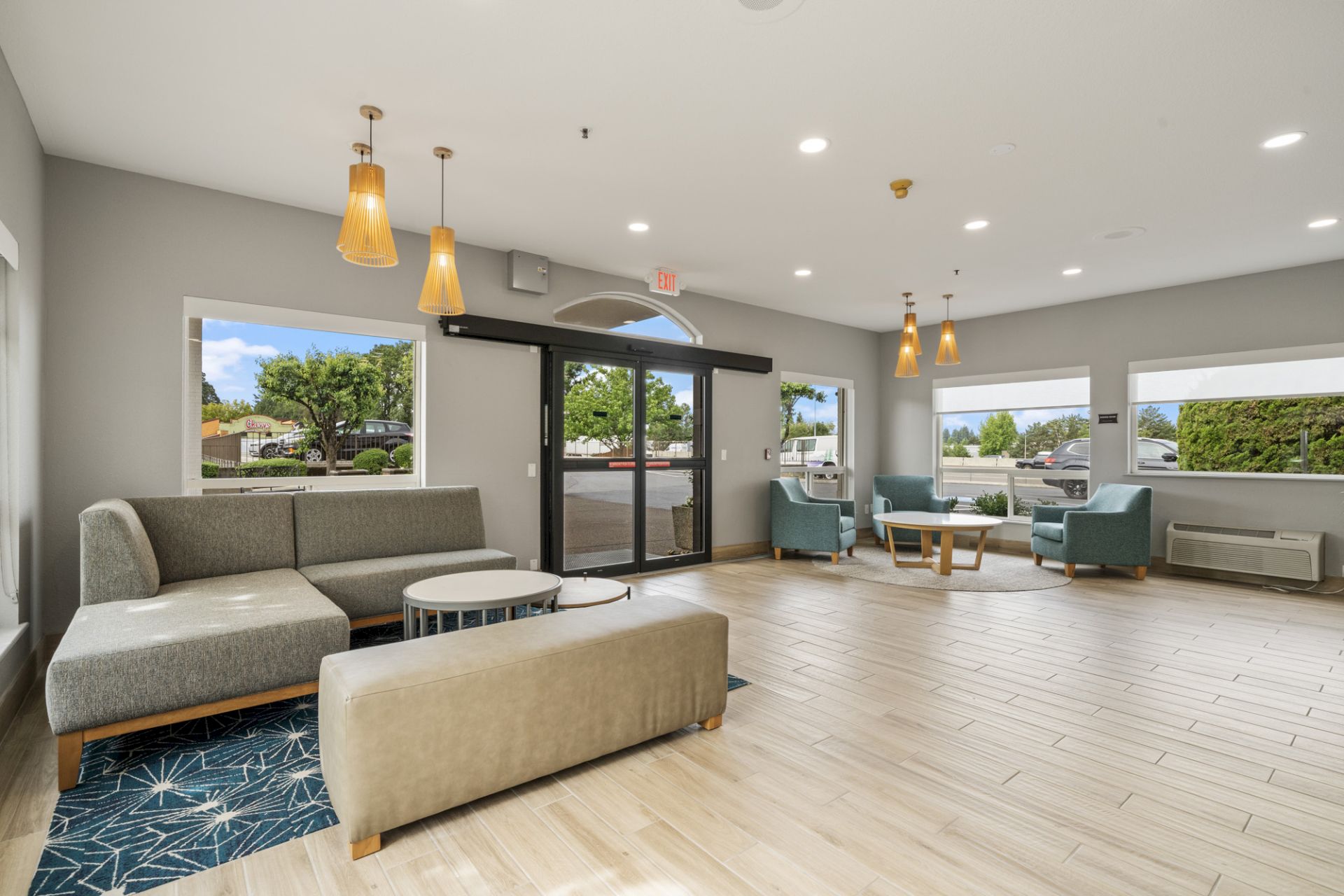 A modern waiting area with multiple seating arrangements, large windows, pendant lights, and a glass entrance door. The d&eacute;cor is minimalist and cozy.
