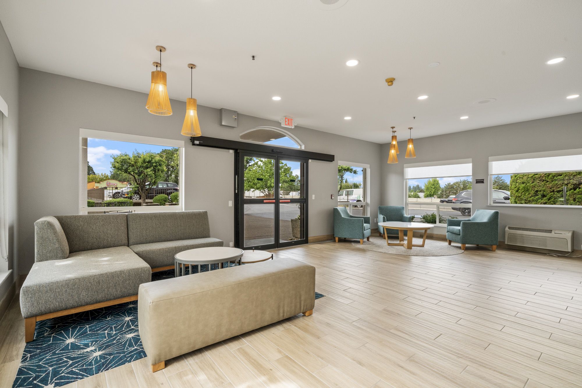 A modern waiting area with multiple seating arrangements, large windows, pendant lights, and a glass entrance door. The décor is minimalist and cozy.