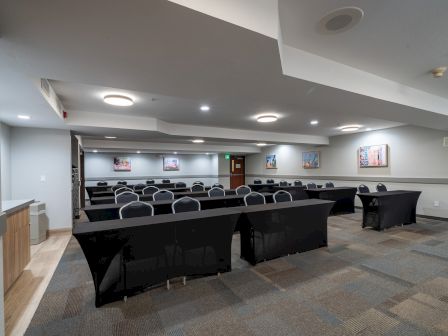 A well-lit conference room with rows of chairs and tables covered with black tablecloths, and some artwork on the walls to add color.