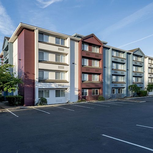 The image shows a multi-story residential building with a mostly empty parking lot in front. The building has a colorful exterior ending the sentence.