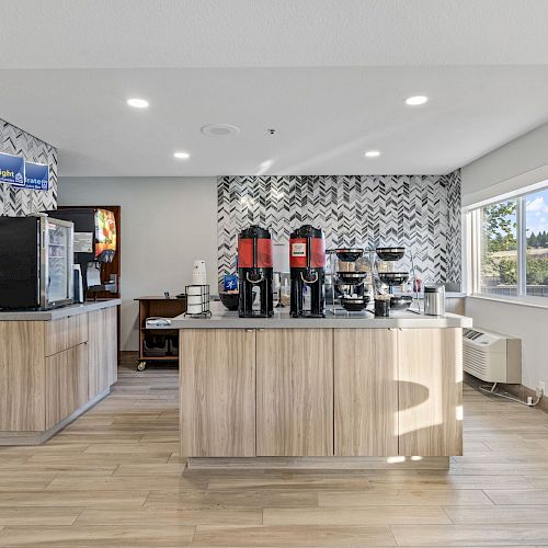 The image shows a hotel breakfast area with coffee machines, a juice dispenser, and a modern design.