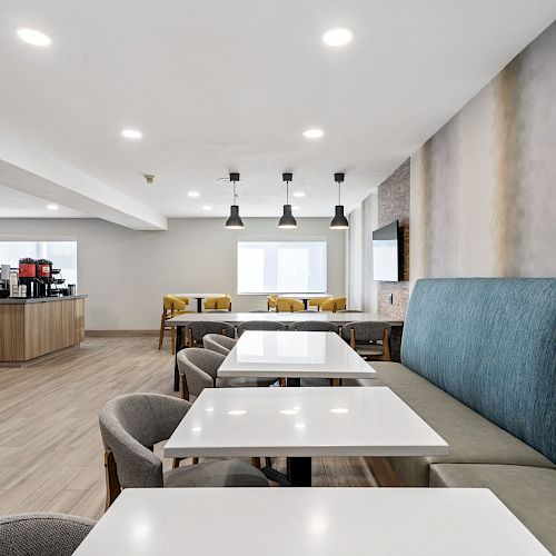 A bright, modern dining area with white tables, blue cushioned seating, and a drink station in the background, featuring wooden accents.