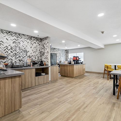 A modern kitchen and dining area with wood flooring, a patterned backsplash, stainless steel appliances, and assorted tables and chairs.