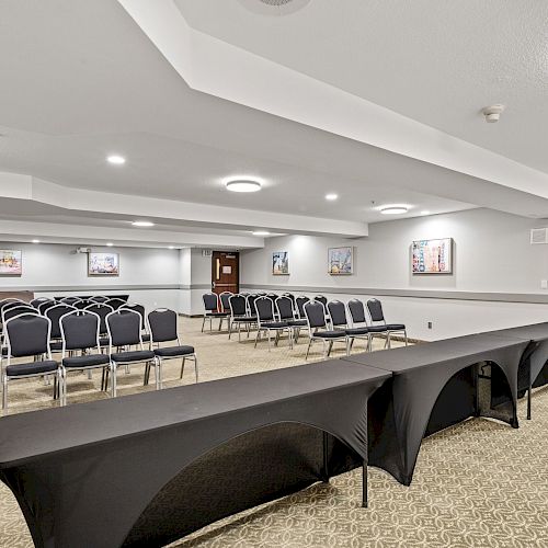 The image shows a conference room with rows of chairs facing a long table covered with a black cloth, and artwork on the walls.