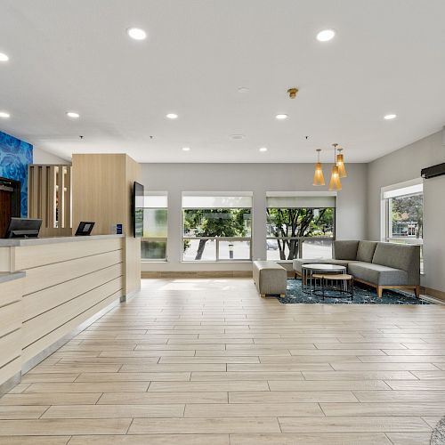 A modern hotel lobby with a reception desk, seating area, large windows, and contemporary decor featuring blue mural art and light wood finishes.