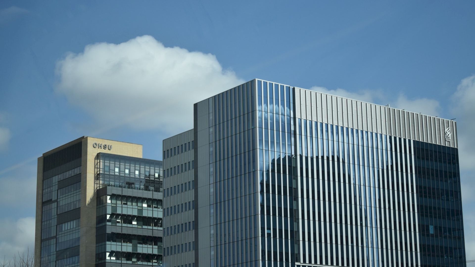 The image shows modern office buildings against a blue sky with some clouds. The architecture is sleek with glass and metal fa&ccedil;ades.