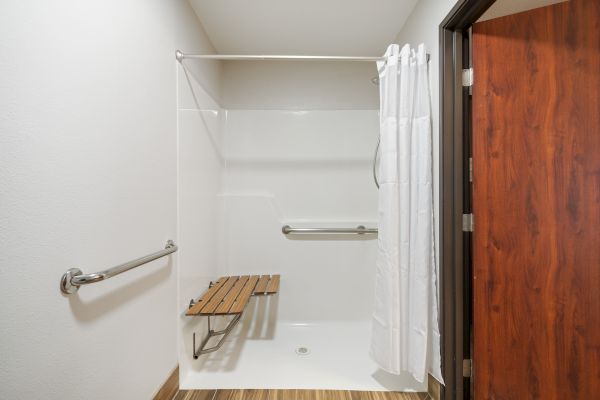 This is an accessible shower with handrails, a wooden bench, and a white shower curtain, designed for ease of use.